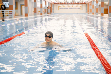 Asian man in hat and goggles swimming in swimming pool