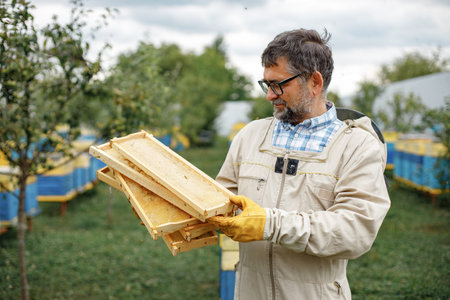 Farmer wearing bee suit holding honeycomb frame and smiling
