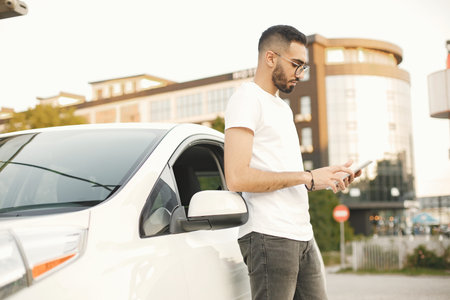 Male driver using a phone while standing near his car