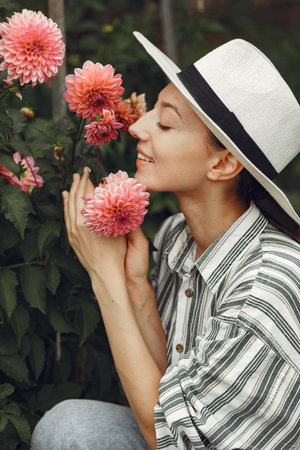 Woman in a hat and gloves standing near pink flowersの写真素材
