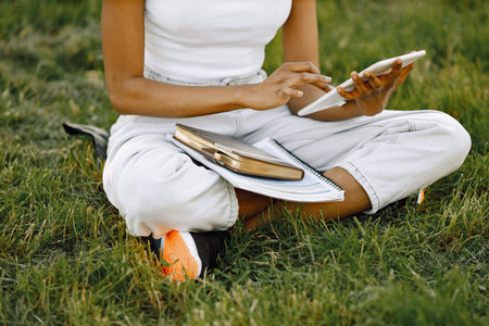 Female african student sitting on a grass and using a tablet