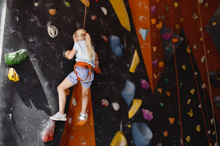 Little girl is climbing up artificial wall wearing safety equipmentの写真素材