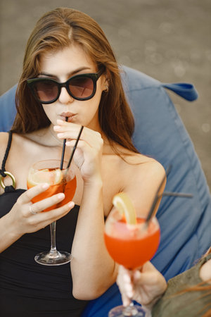 Cropped photo of a girl and her friend in swimwear who drinking cocktails and talking