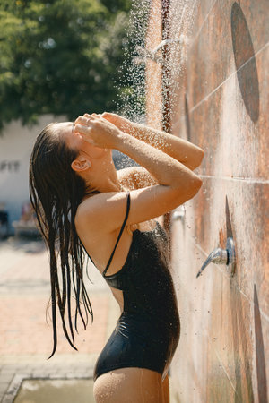 Caucasian woman posing in a swimwear under a shower outdoorsの写真素材