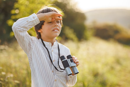 Little boy standing in a field with a binoculars at summerの写真素材