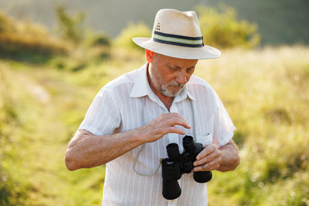 Senior man standing in a field with a binoculars at summerの写真素材