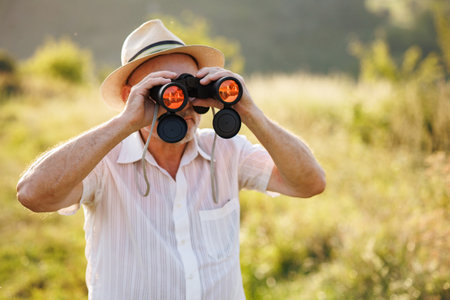 Senior man standing in a field with a binoculars at summerの写真素材
