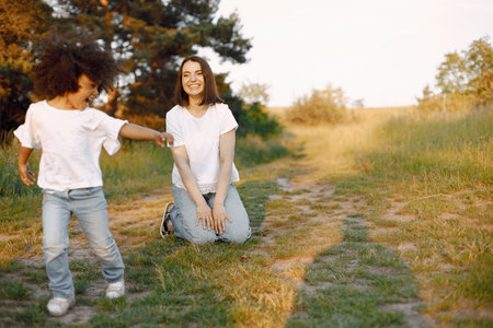 Caucasian mother sitting on a grass and her mixed race daughter runningの写真素材