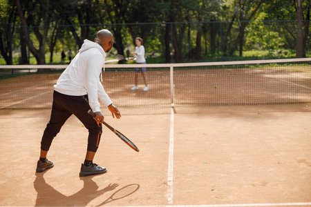 Black man and woman playing tennis at courtの写真素材