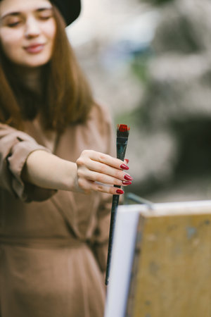 Girl in dress and black hat painting on an easel in a parkの写真素材