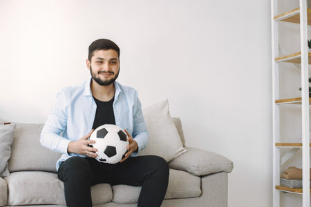 Brunette guy sitting on a coach and watching football at home