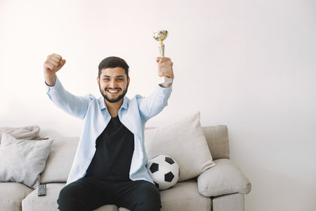 Brunette guy sitting on a coach and watching football at homeの写真素材