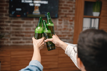 Cropped photo of a bottles of beer in mens hands watching a football gameの写真素材