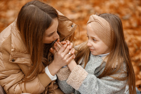 Mother and her daughter sitting on a fallen leaves in autumn forestの写真素材