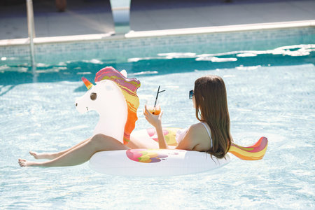 Portrait of a young girl in a swimwear on a unicorn swim ring in the pool