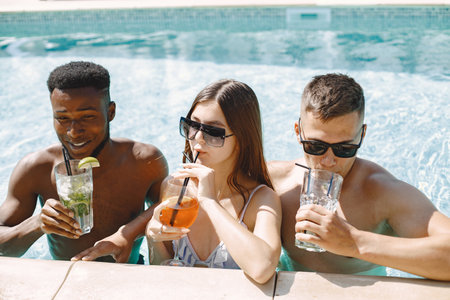 Three friends in a swimwears relaxing with a cocktails near swimming poolの写真素材