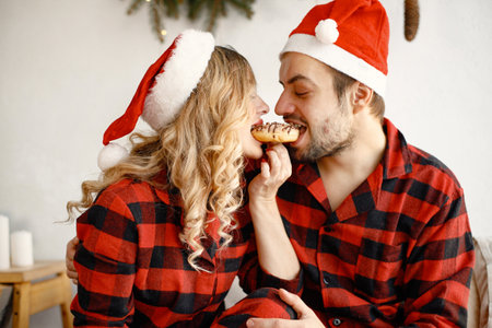 Couple wearing christmas plaid red pajamas sitting on the bedの写真素材
