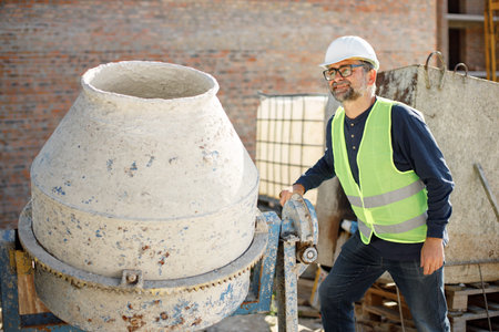 Worker in white helmet at a construction site standing near concrete mixer