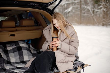 Portrait of a female teenager sitting in an open cars trunk in winter forestの写真素材