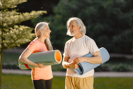 Senior couple with exercise mats standing at park and talkingの写真素材