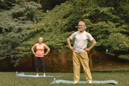Senior couple standing at summer park and doing excercises on a yoga mats