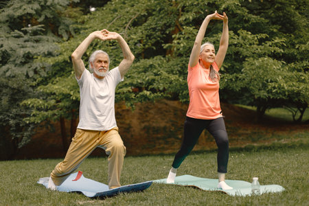 Senior couple standing at summer park and doing excercises on a yoga matsの写真素材