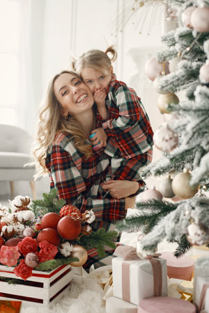 Mom and daughter in plaid pajamas hugging near Christmas treeの写真素材