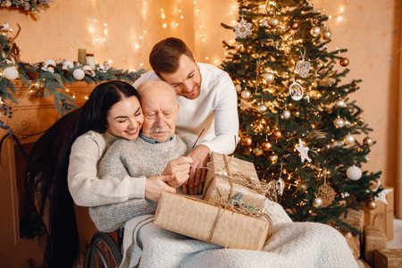Young man, woman and their old father on a wheelchair sitting near Christmas treeの写真素材