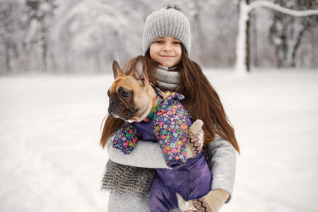 Girl in knitted hat playing with her dog french bulldog on a snowの写真素材