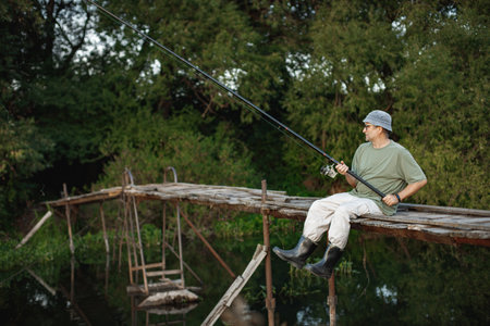 Fisherman with fishing rod on a footbridge near the lake at summerの写真素材