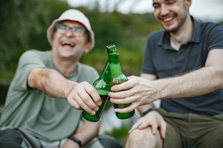 Cropped photo of a men near the lake clinking with two bottles of beerの写真素材
