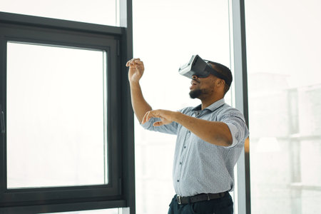 Black male entrepreneur standing near big windows wearing virtual reality glasses