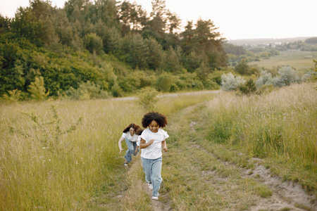Caucasian mother and two her mixed race daughters running on a fieldの写真素材