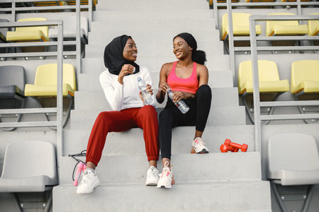 Two black women sitting on a stairs on a stadium after doing workout
