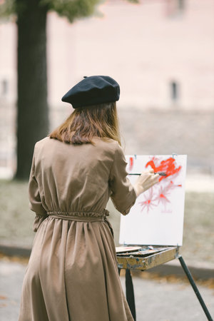 Girl in dress and black hat painting on an easel in a park