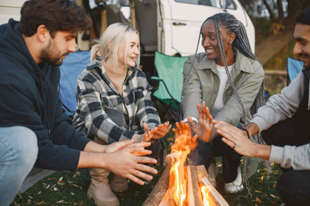 Young friends warming hands by fire at forestの写真素材