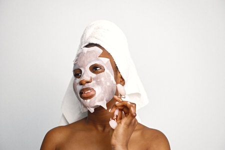 Girl with towel on a head has sheet mask isolated on white backgroundの写真素材