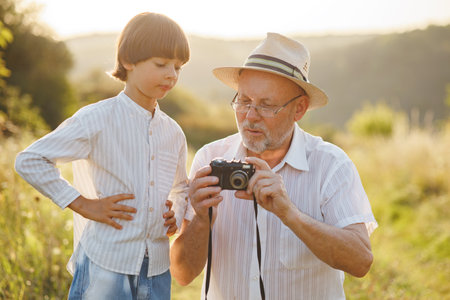 Little boy with his grandfather standing in a field with a camera at summerの写真素材