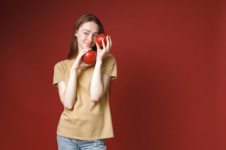 Studio portrait of a girl holding two red apples isolated on red backgroundの写真素材