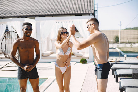 Three people in swimwear enjoying time by a poolの写真素材