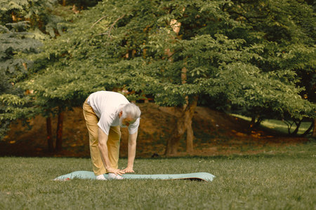 Senior man standing at summer park and doing excercisesの写真素材
