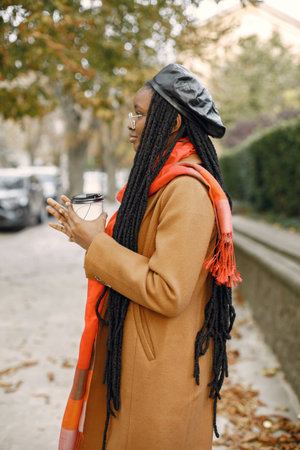 Young black woman in a coat drinking coffee outside