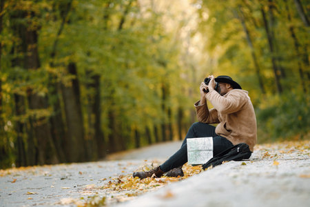 Black man sitting on a road and holding a camera and a mapの写真素材