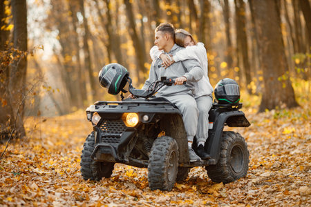 Man and woman hugging on a quad bike in autumn forestの写真素材