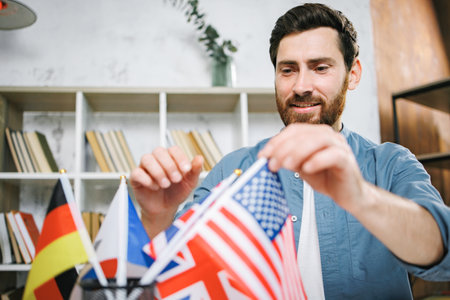 Bearded male tutor sitting on table with different flags and choose someの写真素材