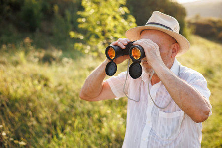 Senior man standing in a field with a binoculars at summerの写真素材