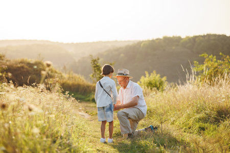 Backside photo of a little boy with his grandfather standing in a field at summerの写真素材