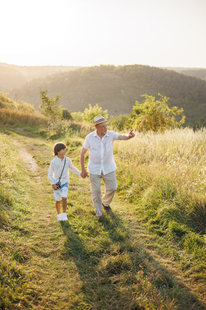 Photo of a little boy with his grandfather walking in a field at summerの写真素材