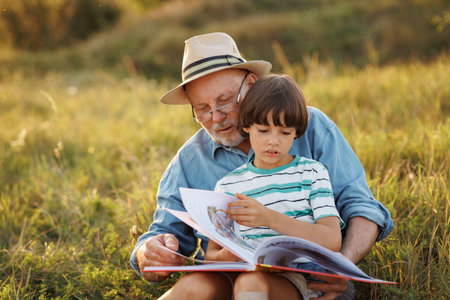 Little boy with his grandfather reading a book in a field at summerの写真素材