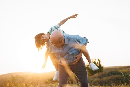 Photo of a senior man carrying a little boy piggyback in a field at summerの写真素材